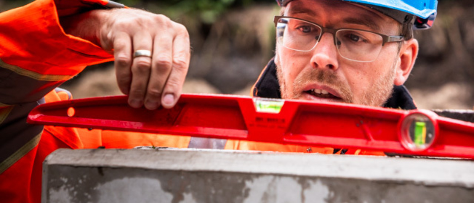 Medewerker op bouwplaats met een waterpas aan het meten