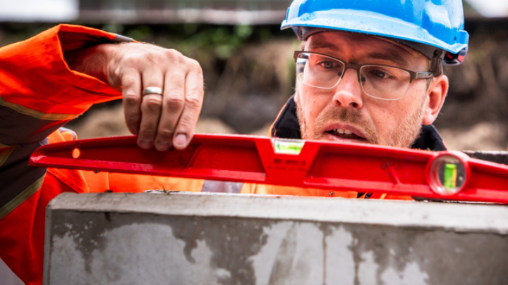 Medewerker op bouwplaats met een waterpas aan het meten